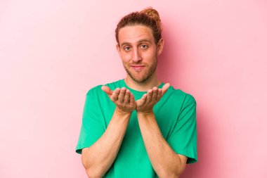 Pembe arka planda izole edilmiş genç beyaz bir adam elinde avuç içi bir şeyle kameraya sunuyor..