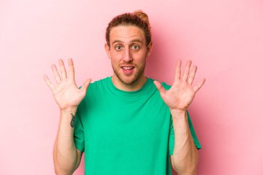 Pembe arka planda izole edilmiş genç beyaz adam hoş bir sürpriz alıyor, heyecanlı ve el kaldırıyor..