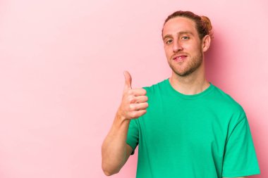 Pembe arka planda izole edilmiş genç beyaz adam gülümsüyor ve başparmağını kaldırıyor.