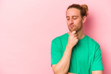 Pembe arka planda izole edilmiş genç beyaz adam şüpheli ve şüpheci bir ifadeyle yana bakıyor..
