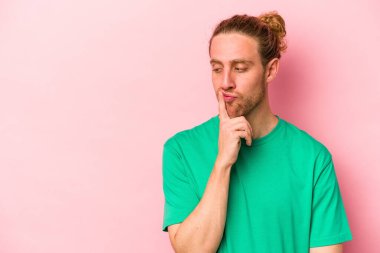Pembe arka planda izole edilmiş genç beyaz adam şüpheli ve şüpheci bir ifadeyle yana bakıyor..
