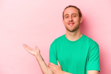 Pembe arka planda izole edilmiş genç beyaz bir adam bir palmiye üzerinde fotokopi alanı ve belinde başka bir el tutuyor..