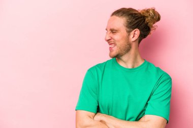 Pembe arka planda izole edilmiş genç beyaz adam kollarını kavuşturarak gülümsüyor..