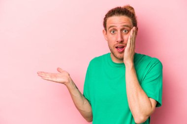 Pembe arka planda izole edilmiş genç beyaz adam, avuç içi fotokopi alanını elinde tutmaktan etkilenmiş..