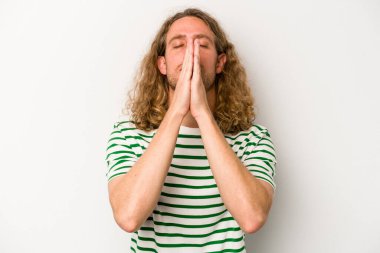 Beyaz arka planda izole edilmiş genç beyaz bir adam el ele tutuşup, ağız kenarında dua ediyor, kendinden emin..