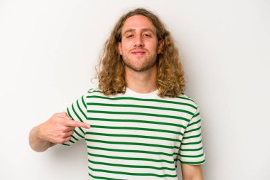 Beyaz arka planda yaşayan beyaz tenli genç bir adam gömlek fotokopi alanını gösteriyor, gururlu ve kendinden emin.