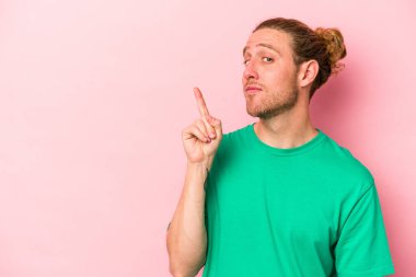 Pembe arka planda izole edilmiş genç beyaz bir adam bir numarayı parmağıyla gösteriyor..