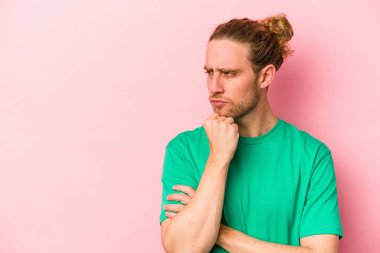 Pembe arka planda izole edilmiş genç beyaz adam rahatlamış bir şeyin fotokopi odasına baktığını düşünüyor..