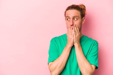 Pembe arka planda izole edilmiş genç beyaz bir adam. Düşünceli bir şekilde ağzıyla ağzını kapatan bir fotokopi odasına bakıyor..