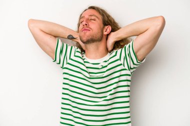 Beyaz arka planda izole olmuş genç beyaz bir adam kendini güvende hissediyor, elleri başının arkasında..