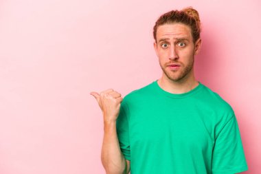 Pembe arka planda izole edilmiş genç beyaz adam işaret parmağıyla fotokopi alanını işaret ederek şok oldu..