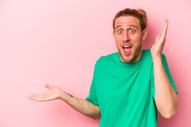 Pembe arka planda izole edilmiş genç beyaz bir adam avucunun içinde fotokopi alanı tutuyor, el üstünde tutuyor. Şaşırmış ve mutlu..