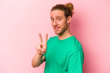 Pembe arka planda izole edilmiş genç beyaz adam zafer işareti gösteriyor ve gülümsüyor..