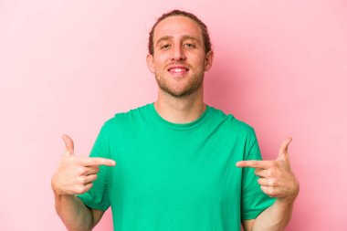 Pembe arka planda izole edilmiş genç beyaz adam parmaklarıyla aşağıya doğru, olumlu bir his..