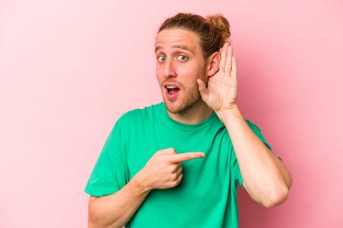 Pembe arka planda izole edilmiş genç beyaz adam bir dedikoduyu dinlemeye çalışıyor..