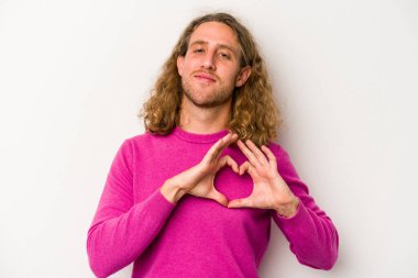 Beyaz arka planda izole edilmiş genç beyaz bir adam gülümsüyor ve elleriyle kalp şekli gösteriyor..