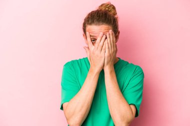 Pembe arka planda izole edilmiş genç beyaz adam parmaklarıyla gözünü kırp korkmuş ve gergin..