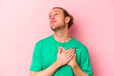 Pembe arka planda izole edilmiş genç beyaz bir adam, dostane bir ifadeye sahip, avuçlarını göğsüne bastırıyor. Aşk konsepti.