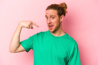 Pembe arka planda izole edilmiş genç beyaz bir adam gömlek fotokopi alanını elle gösteriyor, gururlu ve kendinden emin.