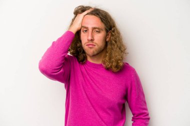 Beyaz arka planda izole edilmiş genç beyaz bir adam yorgun ve uykulu bir şekilde elini başının üstünde tutuyor..