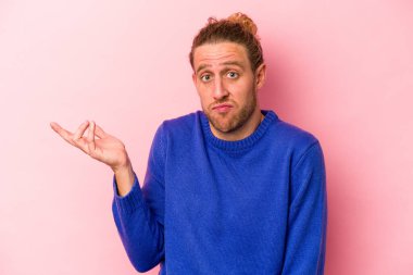 Pembe arka planda soyutlanmış genç beyaz bir adam sorgulama sırasında omuz silkiyor ve şüphe duyuyor..