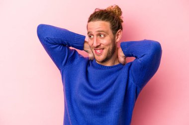 Pembe arka planda izole edilmiş genç beyaz bir adam kendini güvende hissediyor, elleri başının arkasında..