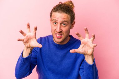 Pembe arka planda izole edilmiş genç beyaz adam gergin elleriyle çığlık atıyor..