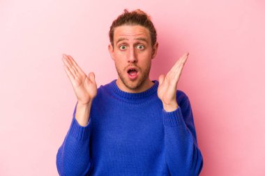 Pembe arka planda izole edilmiş genç beyaz adam şaşırdı ve şok oldu..