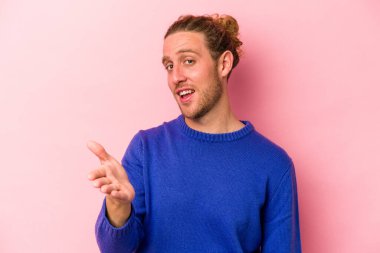 Pembe arka planda izole edilmiş genç beyaz adam selamlama jesti olarak kameraya elini uzatıyor..
