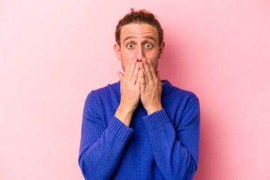Pembe arka planda izole edilmiş genç beyaz adam elleriyle ağzını kapatırken şok oldu..