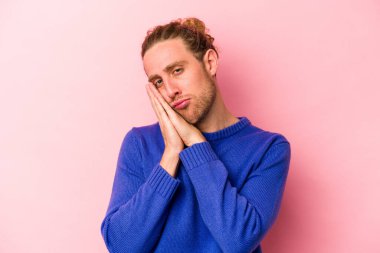 Pembe arka planda izole edilmiş genç beyaz adam esniyor. Ağzı eliyle kapatan yorgun bir hareket sergiliyor..