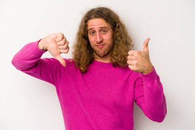 Beyaz arka planda izole edilmiş genç beyaz bir adam baş parmaklarını aşağı ve yukarı kaldırıyor, zor seçim konsepti