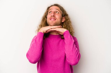 Beyaz arka planda izole genç beyaz adam ellerini çenesinin altında tutuyor, mutlu bir şekilde yana bakıyor..