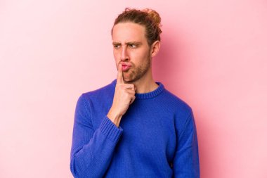 Pembe arka planda izole edilmiş genç beyaz bir adam ya sır saklıyor ya da sessizlik istiyor..