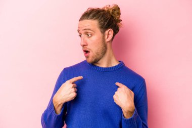 Pembe arka planda izole edilmiş genç beyaz adam parmağını göstererek şaşırdı, geniş bir gülümsemeyle..