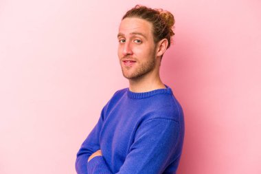 Pembe arka planda izole edilmiş genç beyaz adam kendini güvende hissediyor, kararlılıkla kollarını kavuşturuyor..