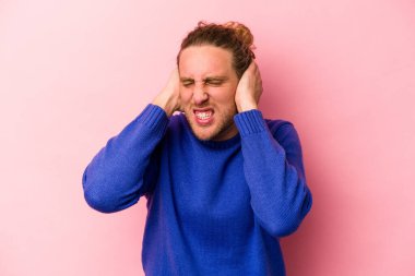 Pembe arka planda izole edilmiş genç beyaz adam kulaklarını elleriyle kapatıyor..