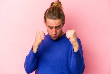 Pembe arka planda izole edilmiş genç beyaz adam yumruğunu kameraya gösteriyor, agresif yüz ifadesi var..