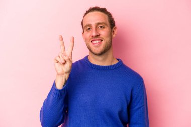 Pembe arka planda izole edilmiş genç beyaz adam iki numarayı parmaklarıyla gösteriyor..