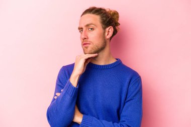 Pembe arka planda izole edilmiş genç beyaz adam şüpheli, belirsiz, seni muayene ediyor..