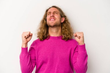 Beyaz arka planda izole edilmiş genç beyaz bir adam zaferi, tutkuyu ve coşkuyu kutluyor, mutlu bir ifade..