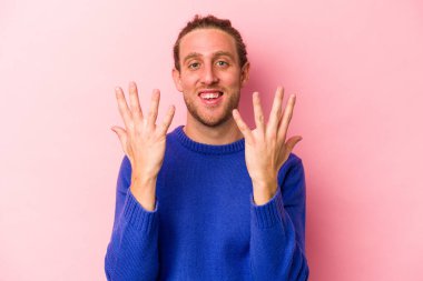 Pembe arka planda izole edilmiş genç beyaz adam on numarayı elleriyle gösteriyor..