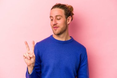 Genç beyaz adam pembe arka planda izole edilmiş neşeli ve kaygısız parmakları olan bir barış sembolü gösteriyor..