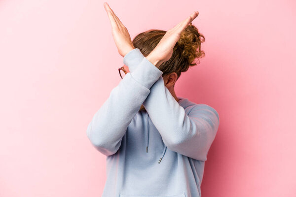 Young caucasian man isolated on pink background keeping two arms crossed, denial concept.