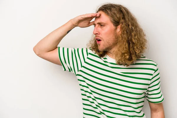 Beyaz arka planda izole edilmiş genç beyaz bir adam uzaklara bakıyor ve elini alnına koyuyor..