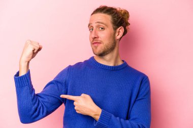 Pembe arka planda izole edilmiş genç beyaz bir adam güçlü bir hareket gösteriyor, kollarıyla, kadınsı gücün sembolü.