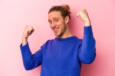 Pembe arka planda soyutlanmış, tasasız ve heyecanlı genç bir beyaz adam. Zafer konsepti.