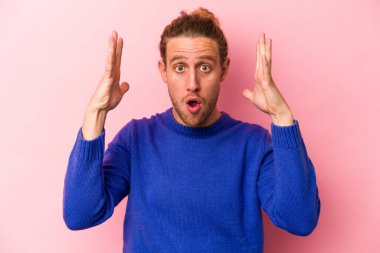 Pembe arka planda izole edilmiş genç beyaz bir adam zaferi ya da başarıyı kutluyor, şaşırıyor ve şok oluyor..