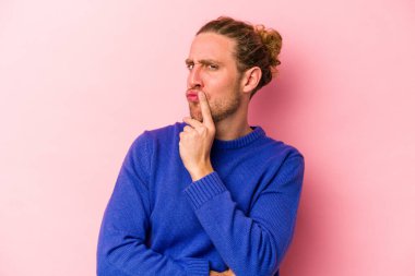 Pembe arka planda izole edilmiş genç beyaz adam alaycı bir ifadeyle kameraya bakıyor..