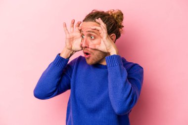 Pembe arka planda izole edilmiş genç beyaz adam bir başarı fırsatı bulmak için gözlerini açık tutuyor..